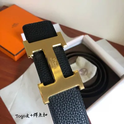 A leather belt with a large gold buckle, resting in an orange gift box