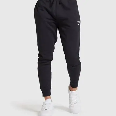 Black tapered joggers worn with white trainers, photographed from the waist down