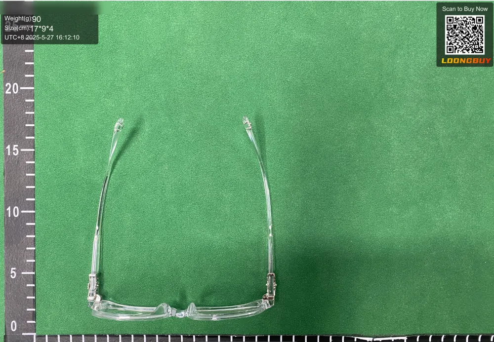 A pair of clear-framed glasses with the arms folded, photographed on the inspection bench beside the ruler