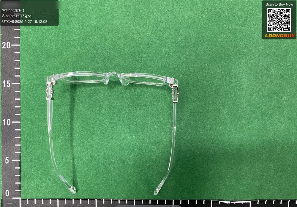 A pair of clear-framed glasses opened flat on a green inspection bench, pressed against a centimetre ruler that runs the full width of the frame