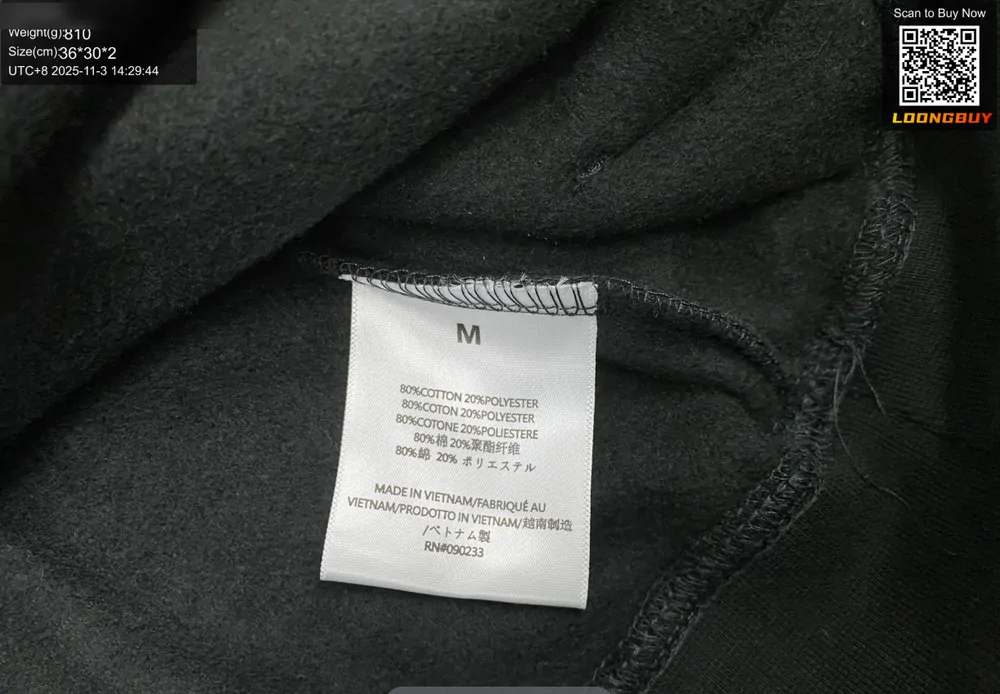 A care label sewn into the side seam of a dark hoodie, photographed close up on the inspection bench