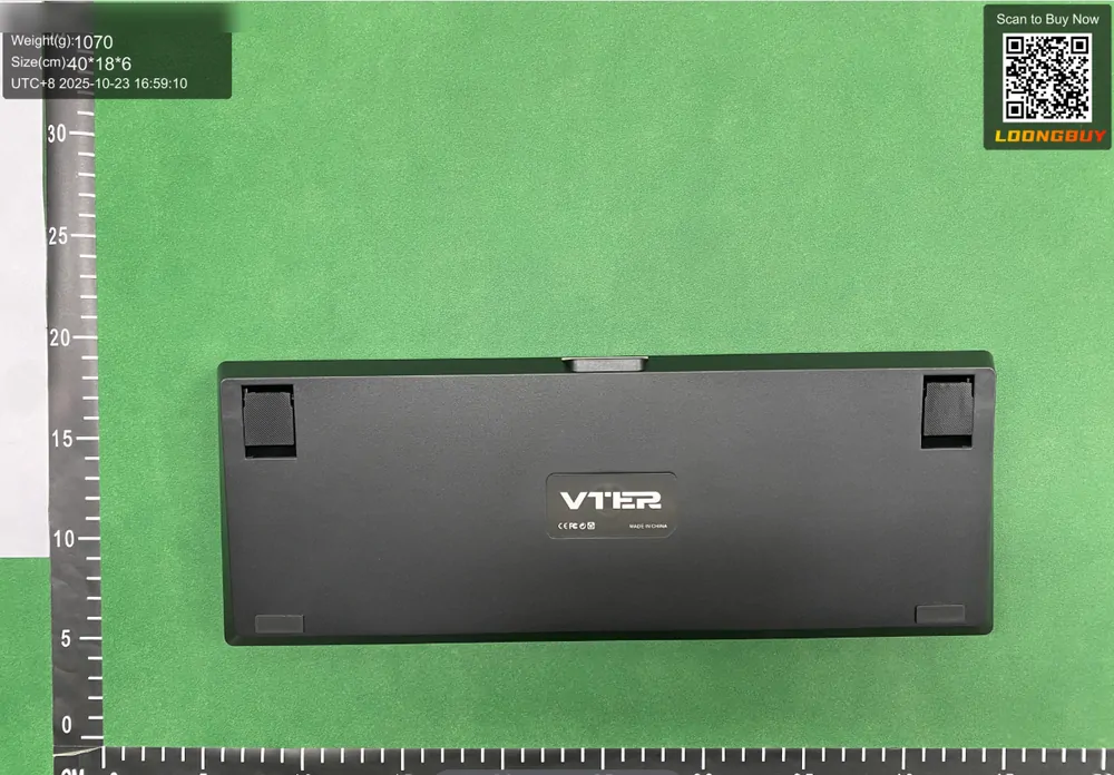 A black mechanical keyboard laid flat on a green inspection bench, with a centimetre ruler below it and a data strip giving weight and box dimensions
