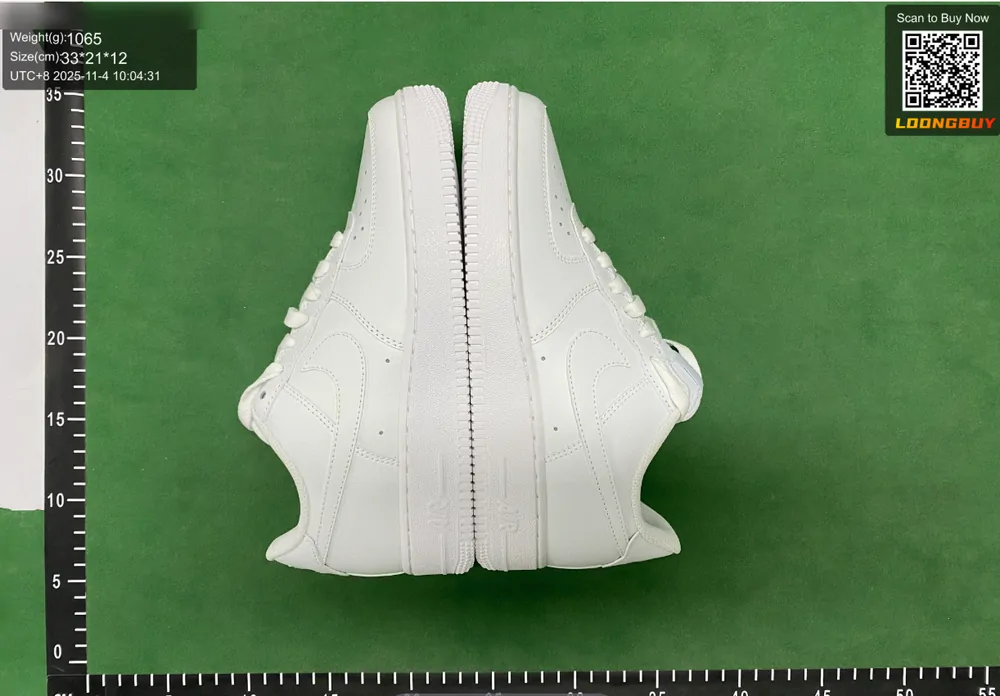 A pair of white sneakers photographed from the side on the inspection bench with the ruler visible below